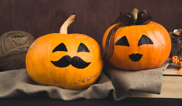 Halloween holiday concept. Funny faces painted on Halloween pumpkins,  decorated with a brown ribbon on a wooden background. A couple of girl and boy. Rustic style