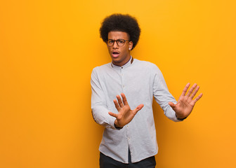 Young african american man over an orange wall rejecting something doing a gesture of disgust