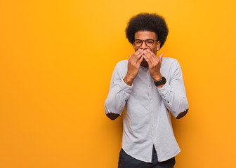 Young african american man over an orange wall laughing about something, covering mouth with hands