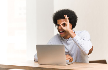 Young black man using his laptop confident doing ok gesture on eye