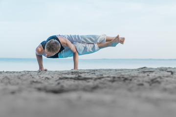Young flexible man standing on hands in yoga position on the seashore beach