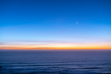 Naklejka na ściany i meble Idyllic scenery at Matanzas beach waves coming from the Pacific Ocean illuminated by a moody sky during twilight. Amazing sea landscape with a colorful sky and a waxing crescent Moon on a starry night