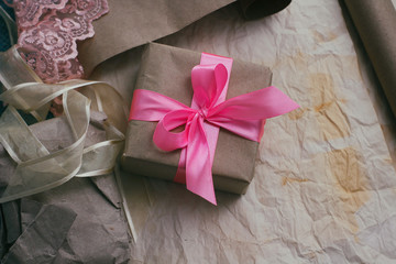 Gift box wrapped in brown craft paper and tied by pink satin ribbon. Packaging process. Gift shop. Wedding decor.