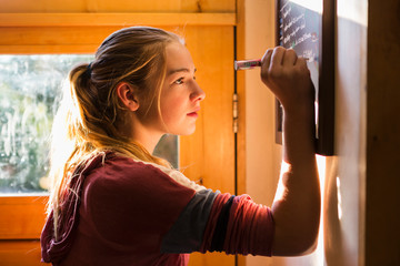 profile of 13 year old girl writing on chalk board, early morning light