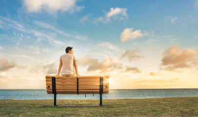 young man sitting on a bench watching the sunrise. 