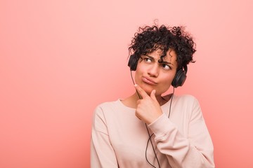 Young african american woman listening to music looking sideways with doubtful and skeptical expression.