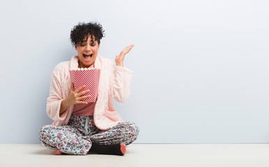 Young african american woman holding a popcorn bucket celebrating a victory or success