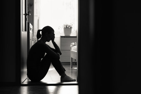 Sad woman sitting alone at home in dark room