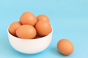 Fresh brown chicken eggs  in the white bowl on light blue background