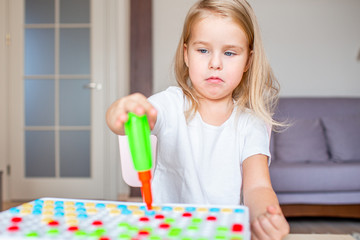 Happy pretty little blonde girl sitting at a table at home playing with a toy screwdriver and multicolor screws. Early education.