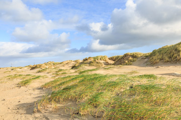 Dune valleys with deep wind holes carved out by heavy storm with swaying marram grasses with scattered clouds against blue sky