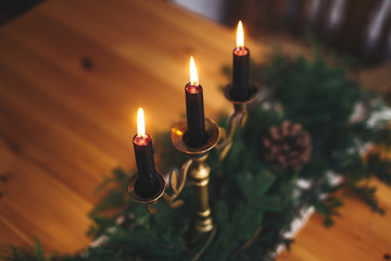 Stylish rustic christmas arrangement for festive dinner. Fir branches with pine cones and vintage candlestick with burning black candles on wooden table. Christmas rural table decor for feast
