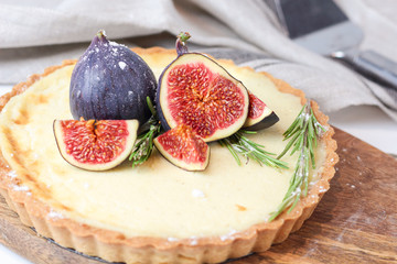 delicious round french classic homemade shortcake pastry dough vanilla custard tart cake decorated with figs and rosemary on wooden plate near with retro fork on grey table cloth. Insta food style