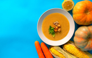 Fresh vegetables and vegetarian autumn pumpkin cream soup on blue background. Copy space. Autumn pumpkin soup  