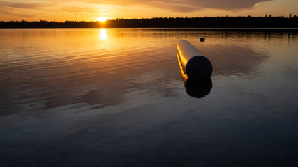 Sunset at the lake romantic with smooth waves and tree trunk in the water and mountains in the background.