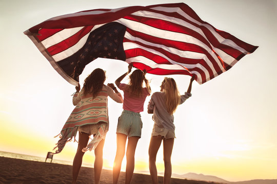 Young friends carrying american flag on the beach