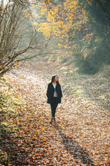 A female model with black coat at forest, behind the model there is a autumn background with yellow, brown and autumn colors