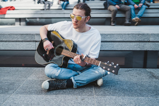 musician is performing outoor, sitting on the floor with people behind