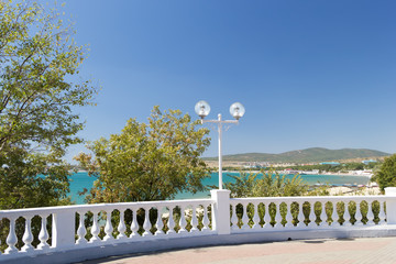 View on seascape through white stone balustrade from promenade on sunny day in Velvet season. Decorative balusters, round lanterns, green trees.