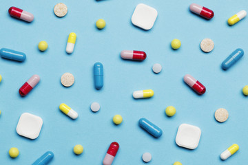 Assorted pharmaceutical medicine pills, tablets and capsules over blue background