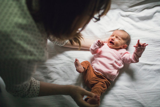 Mother tending to crying baby on bed.