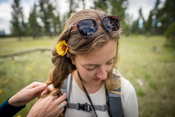 Closeup of young women with flower in hair being braided in nature