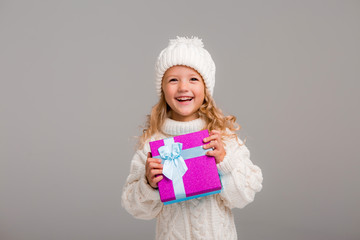 little blonde girl in winter white winter hat smiling holding a pink gift box