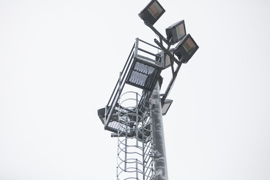 Lighting pole with halogen floodlight and  lightning conductor on the top of it. Metal construction with illuminator. Lighting coverage of a large area. City and urban illumination.