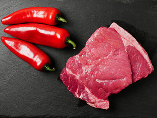 Portion of raw Sirloin steak plate and three red chilly peppers on a slate on a wooden table, Top view.