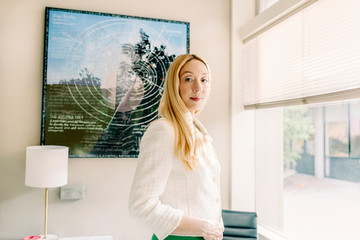 Serious Woman looking at camera standing by window at office