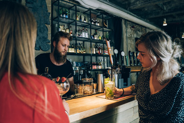 Two Girlfriends And Barman In A Cocktail Bar.
