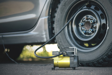 Car wheel and a air pump on the asphalt road close up background.