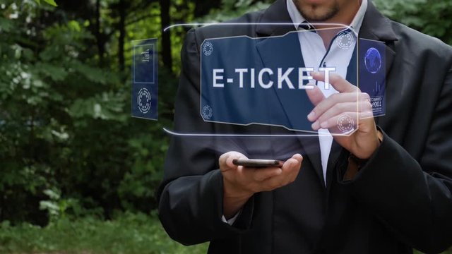 Unrecognizable businessman activates conceptual HUD holograms on smartphone with text E-ticket. Bearded man in a white shirt and a jacket with a holographic screen on a background of green trees