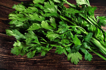 Green celery leaves used as herb, on dark wooden board, closeup photo