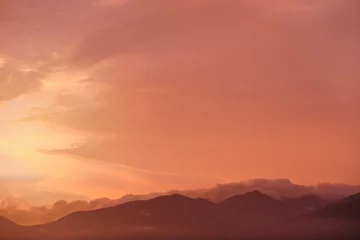 Fototapeten Orange and pink sky after sunset, silhouettes of mountains below - can be used as background with subjects placed in front © Lubo Ivanko