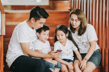 Asain family play game at home - father and Mather teach son and daughter on smartphone