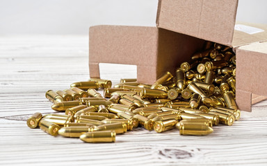 Yellow brass gun ammo spilled from paper carton box on white boar desk - close up - obrazy, fototapety, plakaty