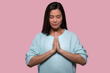 Beautiful brunette woman putting hands together to meditate in peace, practicing spiritual zen, relaxing state of mind