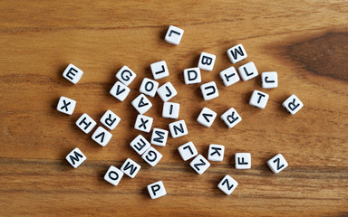 Small white cube beads with various letters scattered on wooden board, view from above