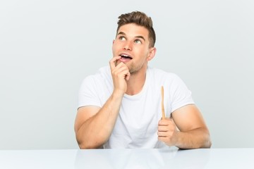 Young man holding a toothbrush relaxed thinking about something looking at a copy space.