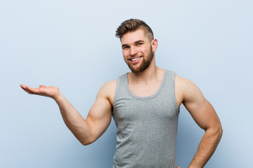 Young handsome fitness man showing a copy space on a palm and holding another hand on waist.