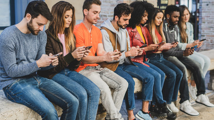 Youth addicted for the smartphone and social media networks. Young people sitting in a bench...