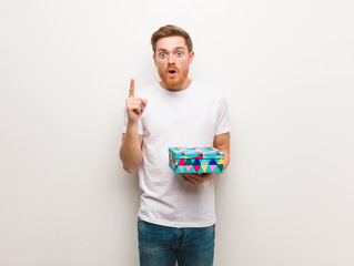 Young redhead man having a great idea, concept of creativity. Holding a gift box.