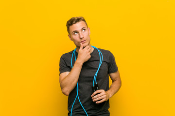 Young caucasian man holding a jump rope looking sideways with doubtful and skeptical expression.