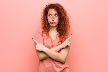 Fototapeta premium Young natural and authentic redhead woman points sideways, is trying to choose between two options.