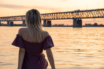 A young, beautiful and slender girl rides on the Amur river. Looking at the big bridge across the river.