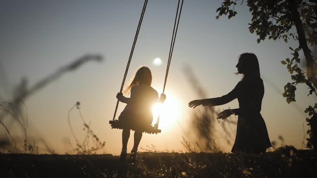 Young mother and her child daughter swinging on the swings and laughing a autumn warm evening outdoors. Happy loving family.