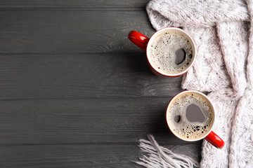 Flat lay composition cups of hot coffee and knitted scarf on grey wooden background, space for text. Winter drink