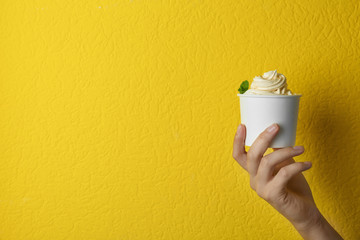 Woman holding cup with tasty frozen yogurt on yellow background, closeup. Space for text