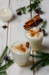 eggnog cocktail in two glasses with christmas decoration on white wooden table